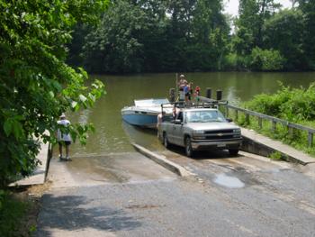 A truck pulling a yacht in a river ramp.